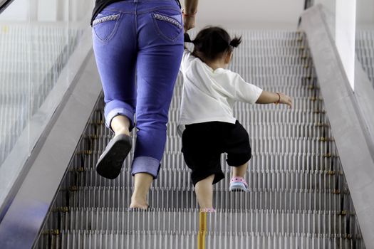 Back view of mother and child walking up together on broken escalator background.