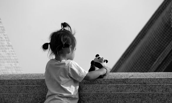 Asian little girl standing on the balcony for a view in the garden with favorite bear. View from the back