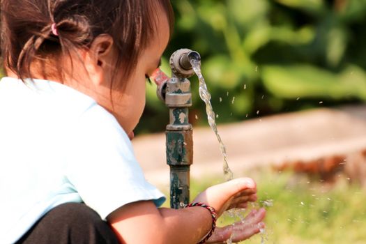 Asian little child girl washing her hands from steel faucets in the garden.