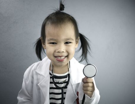 Asian little girl role playing doctor occupation wearing white gown uniform and holding a stethoscope. Playing is learning of children.