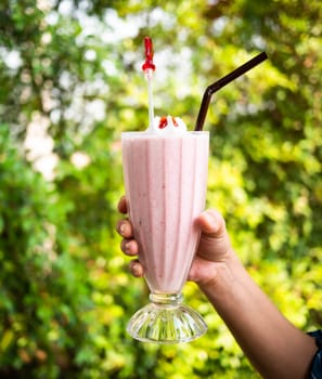 Close-up hand of woman holding strawberry smoothie in clear glass. over nature background.