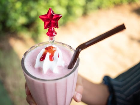 Close-up hand of woman holding strawberry smoothie in clear glass. over nature background.