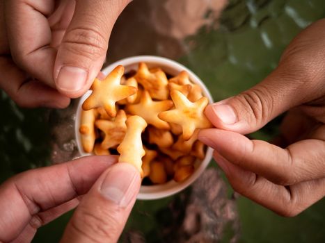 Close-up of hand hold healthy low calorie animal crackers in small cup placed on glass table.