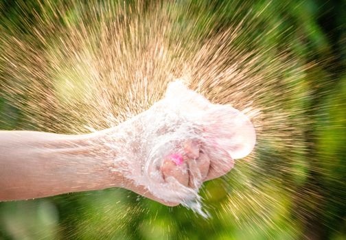 Close-up of hand squeeze the balloons that water inside and splashing aruond it; on blurred nature background in the garden.