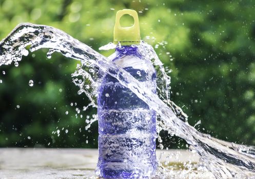 Fresh pure water splashing around of bottle with blurred background. Selective focus and space for text.