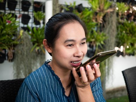 Joyful Asian young woman talk on the speaker phone with smiley face in coffee cafe.