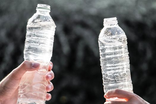 Hand holding fresh pure water bottle on blurred background. Selective focus and space for text.