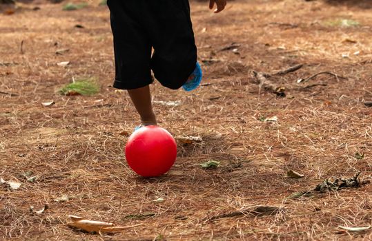 Close-up legs of Asian little child playing football in the park.