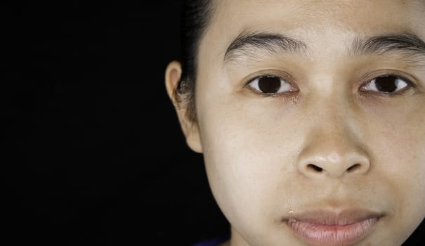 Close-up of The face of an Asian young woman who doesn't have makeup; isolated on black background.