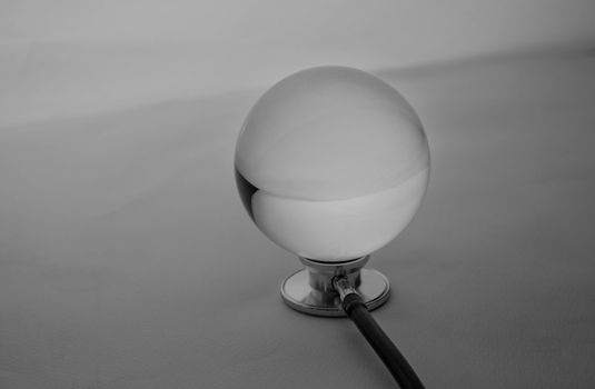 Crystal glass ball sphere placed on medical stethoscope on grey gradient background.