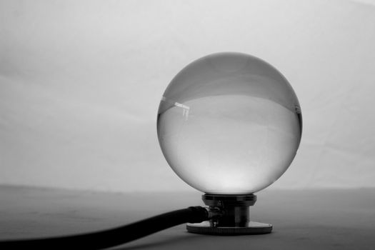 Crystal glass ball sphere placed on medical stethoscope on grey gradient background.