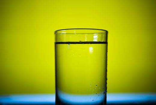 Cold water in clear glass on yellow background.