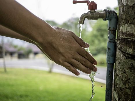 Close up hand of Asian teen boy washing his hands from steel faucets in the garden.