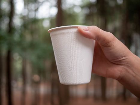 Close-up of hand holding hot beverage in paper glass in the morning on blur nature background. Relaxation travel concept.