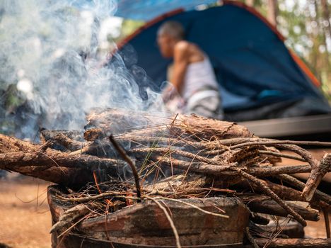 Asian family on camp with firewood in the old Thai traditional stove with smoke at camping spot in a pine forest. Selective focus.