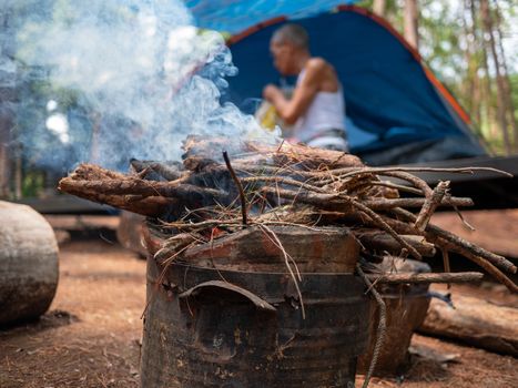 Asian family on camp with firewood in the old Thai traditional stove with smoke at camping spot in a pine forest. Selective focus.