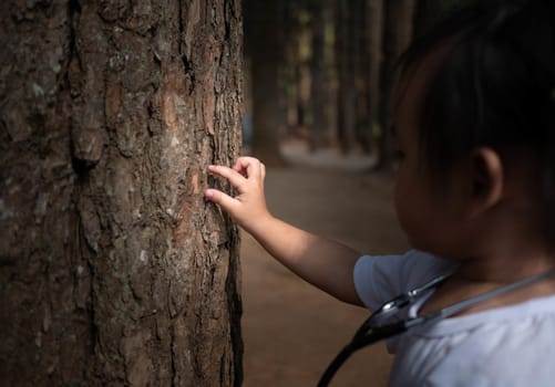 Asian little child girl hand listening a tree with a stethoscope to explore and save environment concept.