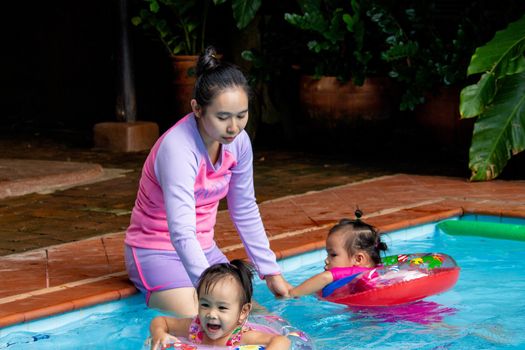 Young Asian mother and her daughter having fun in swimming pool.