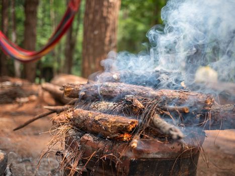 Asian family on camp with firewood in the old Thai traditional stove with smoke at camping spot in a pine forest. Selective focus.