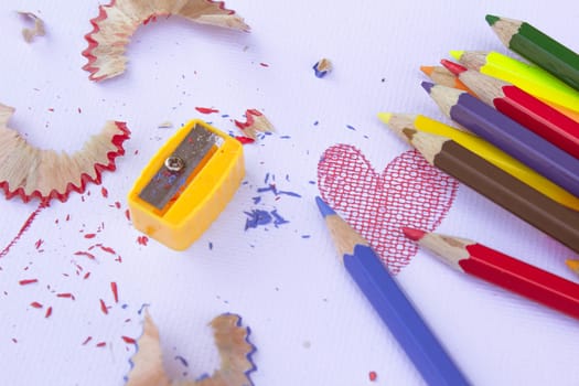 Colorful group of pencil crayons, sharpener and shavings from sharpening on a white paper background. Education frame concept.