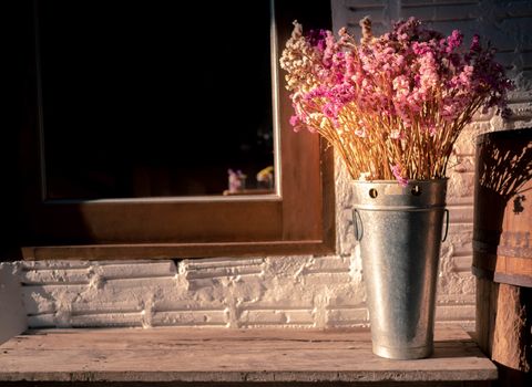 Dried flowers in stainless steel tanks on wooden chair nearing the window with sunlight in evening. Background concept.