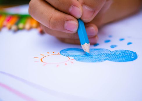 Close up hand of painting Clouds, rain and sun on white paper background. Education concept.