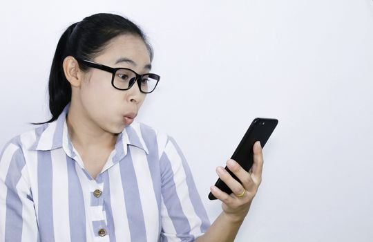 Business Asian young woman waring glasses looking smartphone over white background, shocked face. Health and medical concept. Space for text.