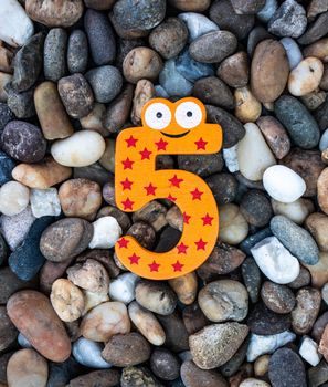 Pebbles pattern or small stones background in garden with colorful Arabic wooden numbers; 5. Concept of new year and textured.