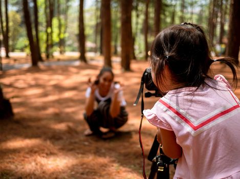 Asian little child use camera is taking photo for her mother at pine forest in Chiang Mai, Thailand. Relaxation travel concept.