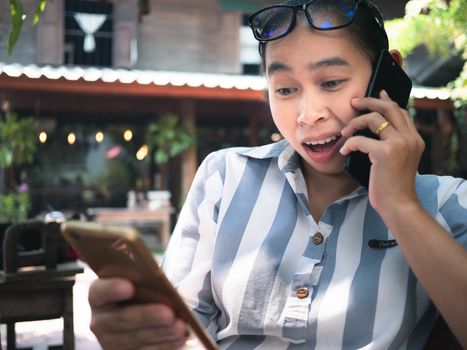 Stressed business Asian young woman holding smartphone for work while talking on the phone at coffee cafe, Unhappy and serious face.