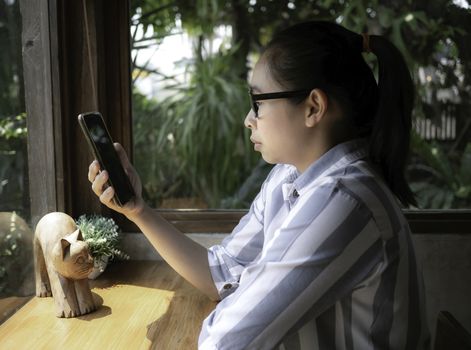 Asian little child is looking cartoon on smartphone happily at food court in mall.