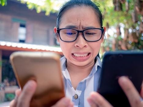 Business Asian young woman holding 2 smartphone do busy with work, Unhappy and worry face.
