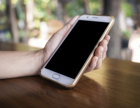 Close up of hand holding smartphone over wooden table background with space for your text.