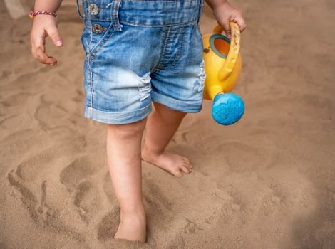 Close up of Asian little girl holding plastic watering can toys in the playground and play a sand with plastic beach toys happily. Playing is learning for children.