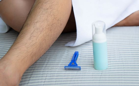 Close-up view of Asian woman shaving leg hair with blue razor and use foam to prevent injury. Body care and  Hair removal concept.