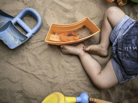 Close up of legs Asian little girl sitting on sand ground in the playground and play a sand with plastic beach toys happily. Playing is learning for children.