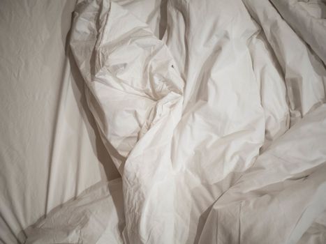 White crumpled blanket on bed with black and white pillow in the morning. Messy bed. Concept of relaxing after morning.