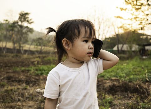 Asian little girl role play talking by phone to mother in the garden with sunset background. Playing is learn for children.