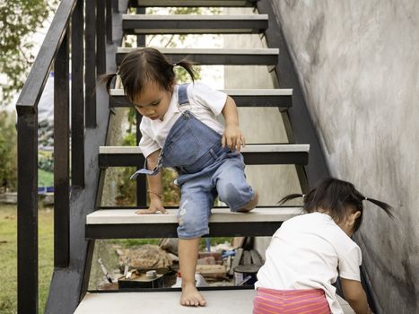 Asian little child and sister try to climb the stairs by herself. Dangerous in children. Education and self-development concept.