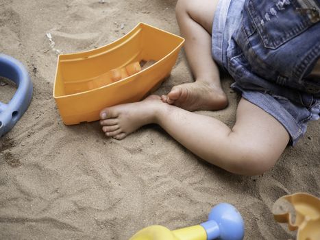 Close up of legs Asian little girl sitting on sand ground in the playground and play a sand with plastic beach toys happily. Playing is learning for children.