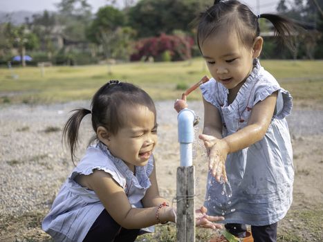 Asian little girl and sister washing her hands from steel faucets in the garden.