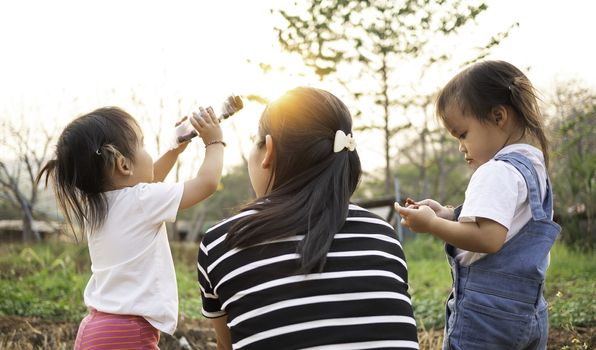 Asian little child girl drink water from bottle after tired of playing in the garden with mother and sister, looking sunset in evening.