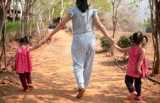 Asian mother and daughters holding hand together and walking in the mulberry garden in the morning.