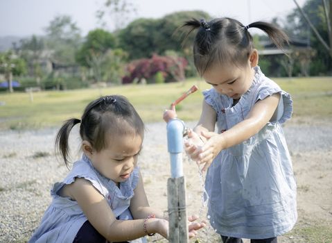 Asian little girl and sister washing her hands from steel faucets in the garden.
