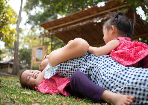 Asian little girl hugging her mother from the back; Pretend mother while lying on grass in the park.