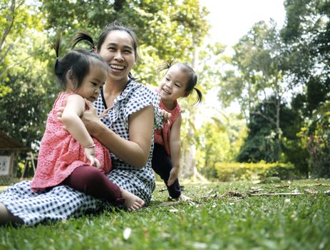 Asian mother and her daughters playing together on grasses ground in the park so happily.