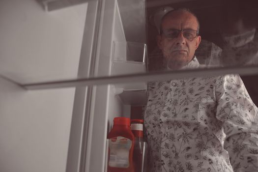 Hungry man looking for a late night meal in an empty fridge. Senior man looking for a snack in the fridge at night, view from the fridge.