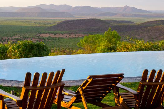 Empty chairs by the swimming pool overlooking the African savannah landscape