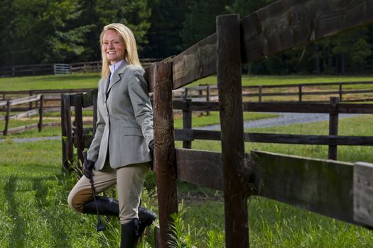 A blonde equestrian model poses outdoors before a horse show