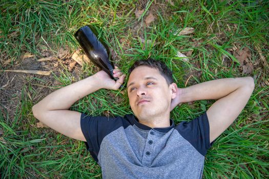 drunk man with a bottle of alcohol in his hand lying on a green field.